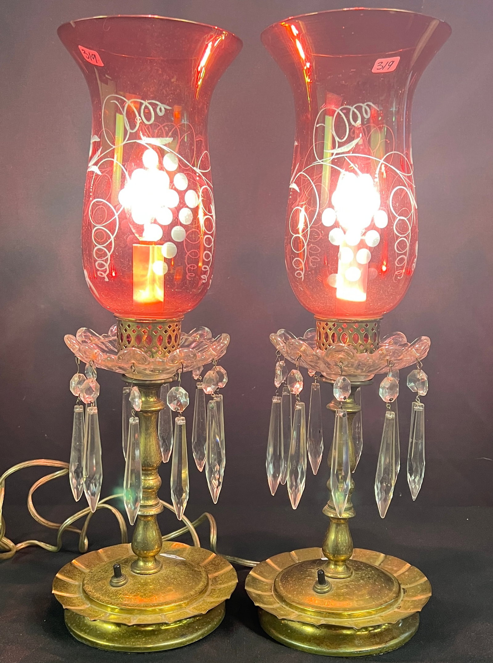 Pair of Cranberry Glass Hurricane Mantel Lamps: A pair of Victorian-revival cranberry glass hurricane mantel lamps, with cranberry red hand-blown glass shades with floral etching, brass bases, and dangling faceted crystal prisms. They have been