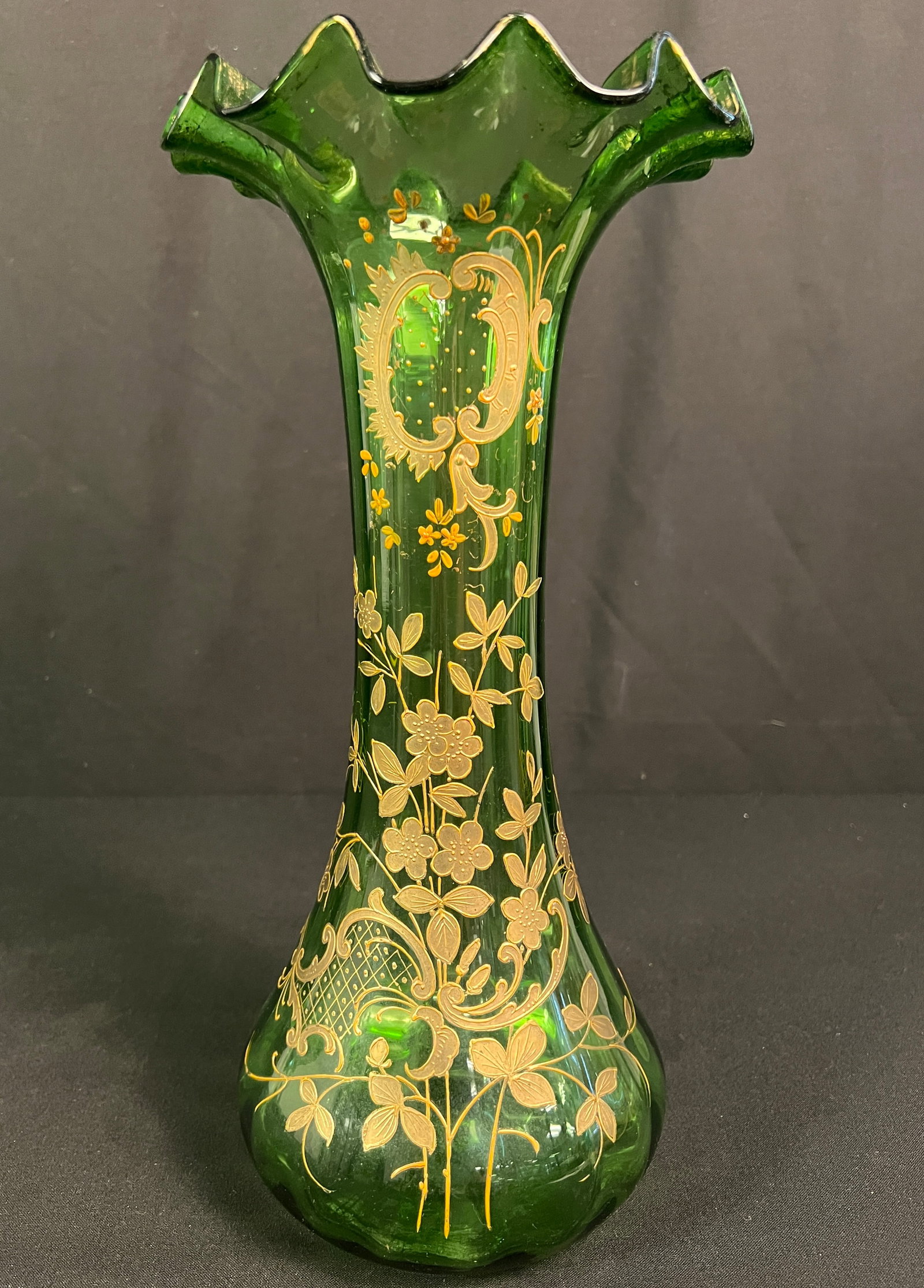 Bohemian Green Art Glass Vase: An antique Victorian-era green art glass vase featuring hand-applied floral enamel decorations, gold gilt highlights, and a ruffled rim. With wear to the gilding on the ruffled rim, this vase is in