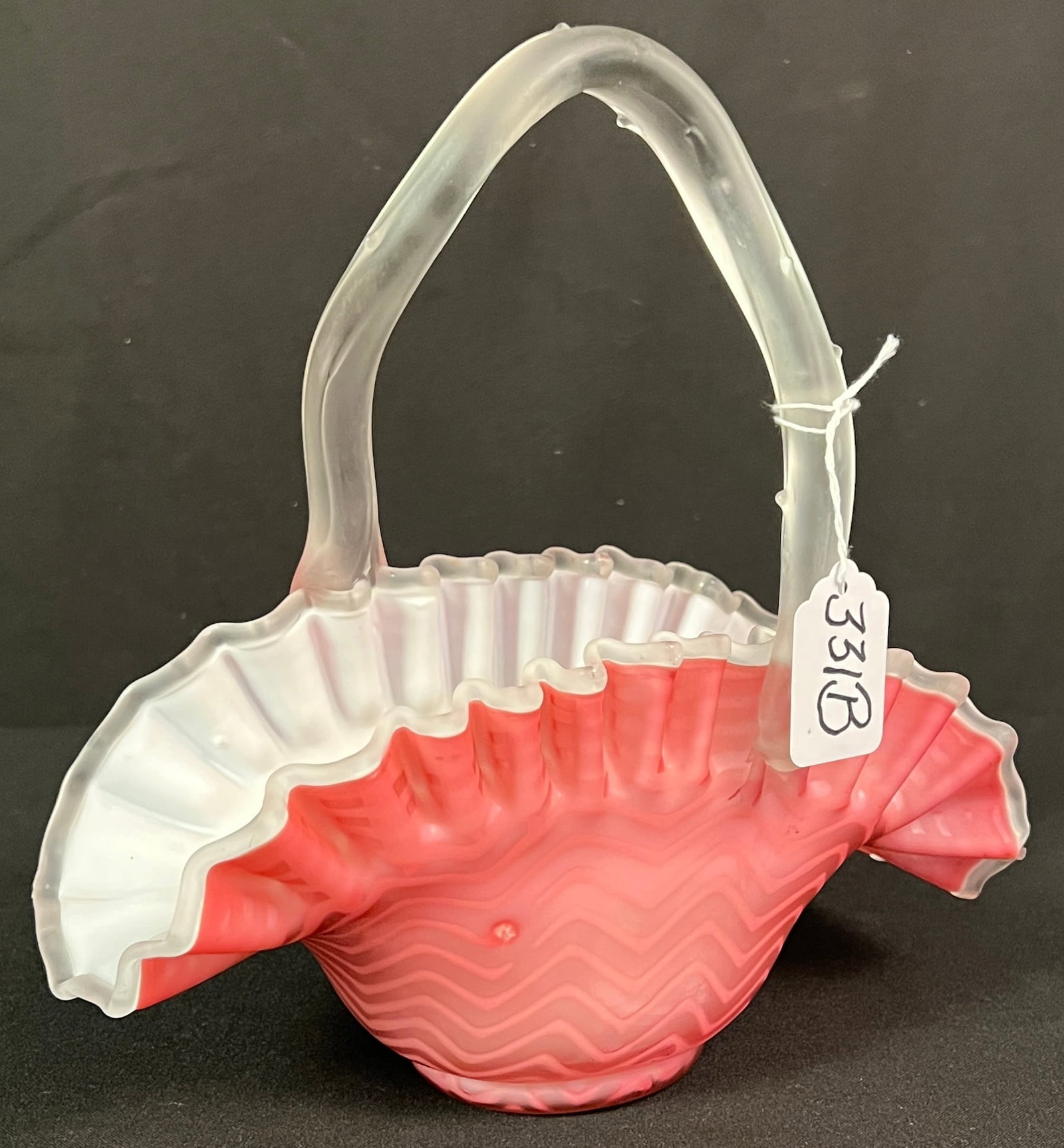 Satin Glass Ruffled Pink Basket: A pink cased and satin glass ruffled edge basket with applied cactus handle with a light chevron pattern. In excellent condition, it measures 10" tall X 9.5" long X 4" across.
