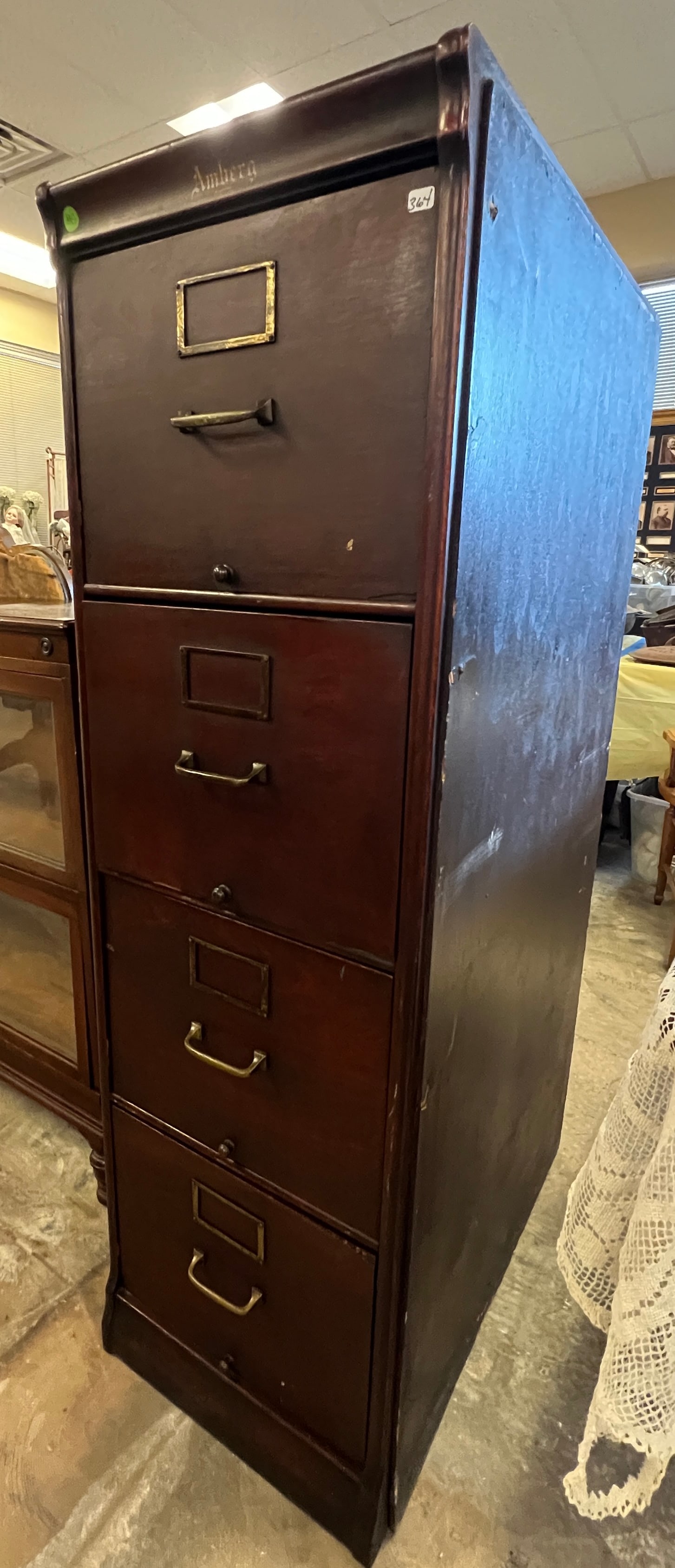 Amberg Four Drawer Filing Cabinet: An Amberg mahogany four drawer filing cabinet from the turn of the century. In its original finish, it retains its brass hardware and sides have been modified. In as found condition, it measures 54"