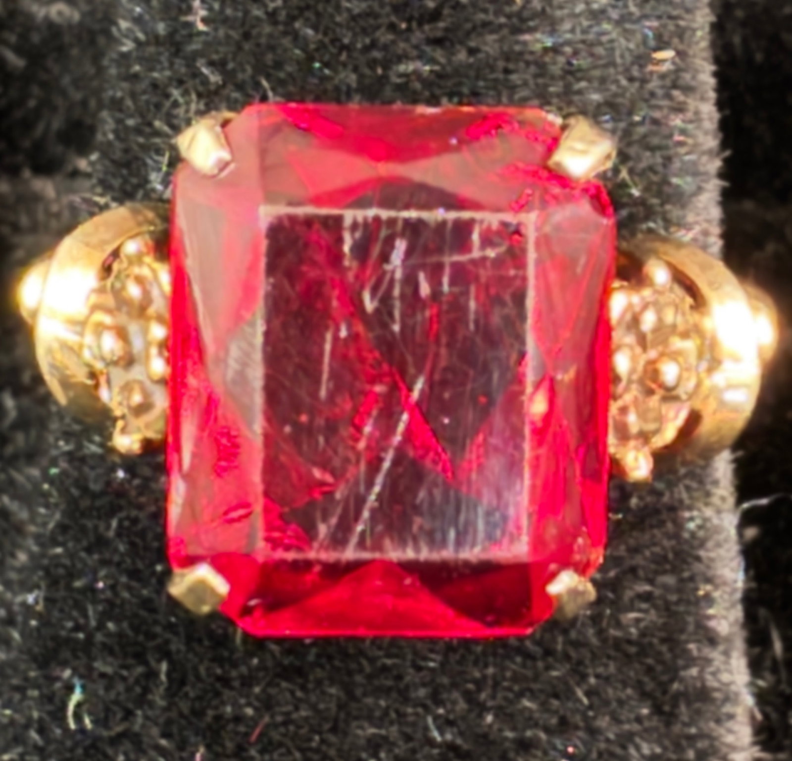 10K Women's Vintage Ring: A 10k women's ring with red glass stone and pierced carved floral setting. This ring likely dates to the 1920s, with some minor age wear to the stone but overall presents nicely. The ring is a size 6 