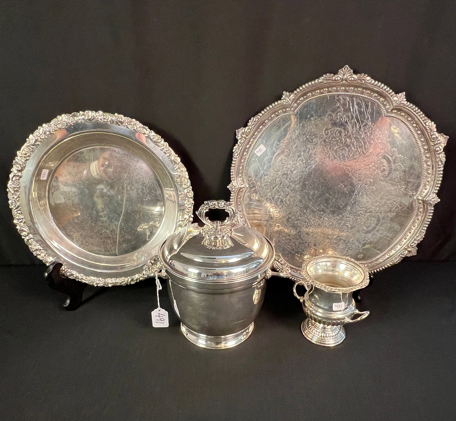 Silver Plate Covered Ice Bucket, Trays and More: A group of silver plate to include a double handled covered ice bucket, a double handled miniature urn, a footed dessert dish with elaborate chased edge, and a round serving tray. All in excellent, ho