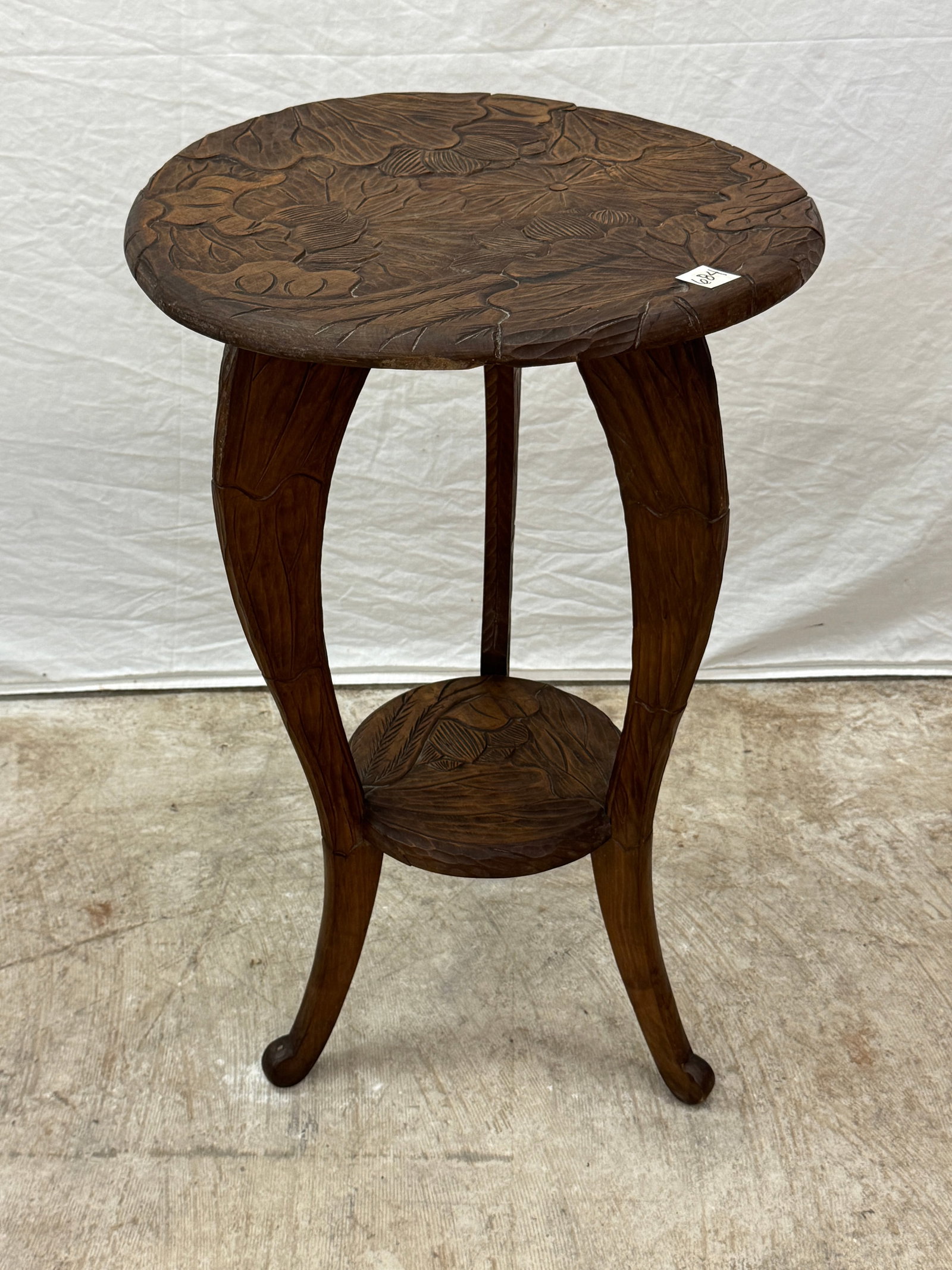 Carved 2 Tiedred Plant Table: A Mid Century 3,legged extensively carved 2 tiered plat table with botanical and floral carvings . Slight warping to top.