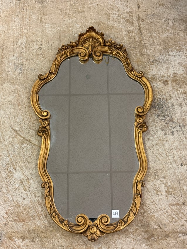 Gilded Wall Mirror C 1930's: A fancy shield shaped gilded wall mirror c 1930's with floral and scalloped accents in good condition (minor losses noted). It measures 34.5" tall X 19.5" across.