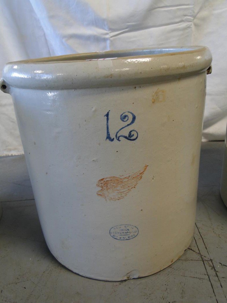 A signed Red Wing 12 gallon bale handled crock missing: A signed Red Wing 12 gallon bale handled crock missing bales. Minor chip on base noted. Medium sized Red Wing mark. It measures 17 1/2" tall by 16 1/2" across