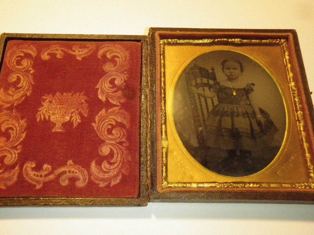 Daguerreotype: shows a young female child standing next to a chair with a necklace on. 3 x 3 3/4".