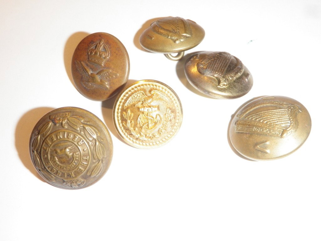 Collection of Buttons: One reads, "The Kings Regiment". There are a total of six buttons in this collection. One has an eagle over an anchor, one has a bird under a crown, three of them show a harp with the letters I on one