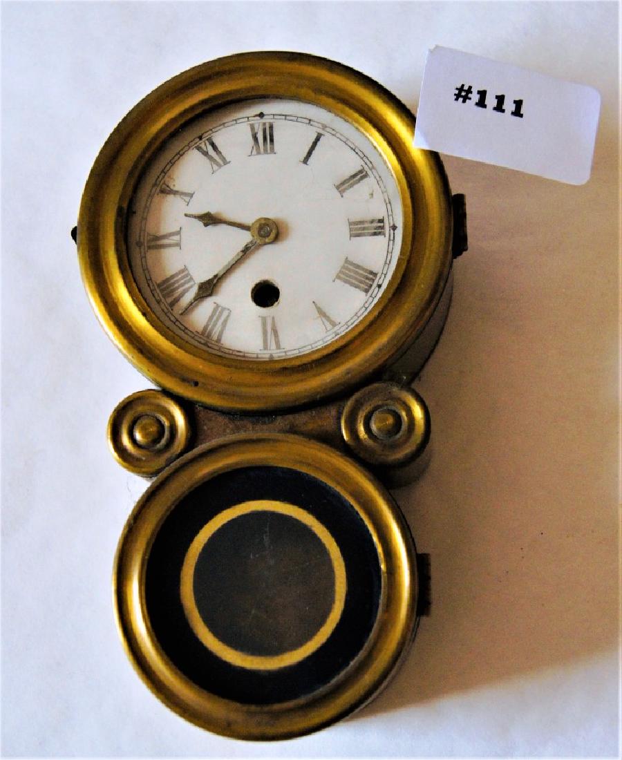 Miniature of an Ingraham "Ionic" wall clock but case is: Miniature of an Ingraham "Ionic" wall clock but case is in turned brass case and having a porcelain dial with roman numerals, top door with clear glass and bottom door with a reverse painted glass wit