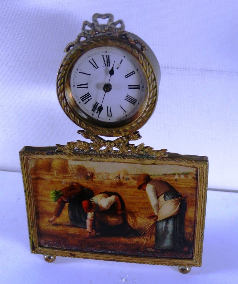 Sm. novelty bras trim clock w/hand wind mech.,: Sm. novelty bras trim clock w/hand wind mech., "Gleaners" motif panel that appears pporcelain at first glance but is a celluloid panel, a pretty clock with ribbon ormolu trim at top and round button f
