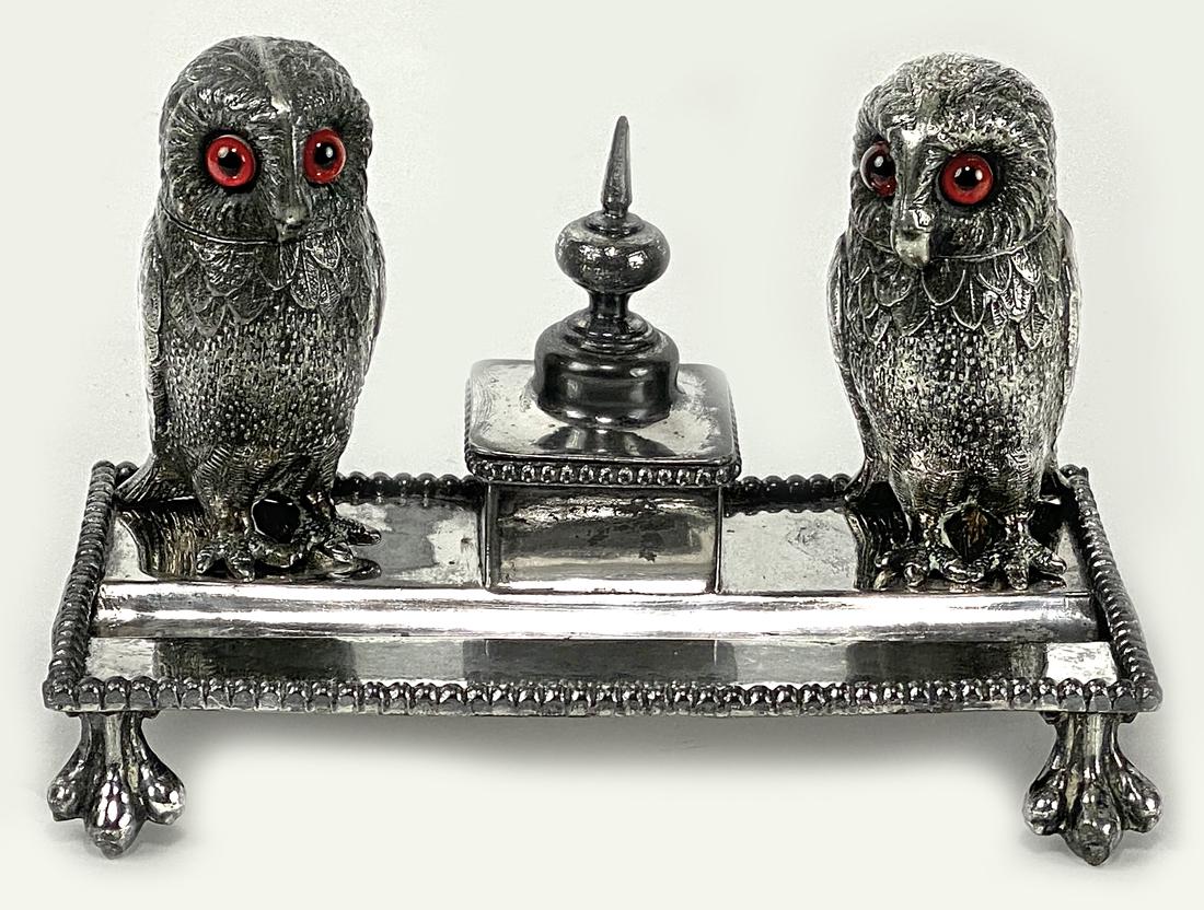 ENGLISH SILVER PLATED OWL INK STAND: 19th c., a pair of owls with glass eyes and original glass inserts, flanking a lidded nib compartment, platform supported by owl feet, 4.5"h; 7"w; 4"d