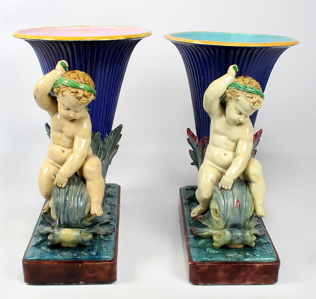LARGE PAIR OF MINTON MAJOLICA FIGURAL PLANTERS: c. 1875, assembled pair, minor differences, each a putto seated on a dolphin supporting a blue cornucopia, 27"h; base 24"w; 10.5"d one impressed MINTON