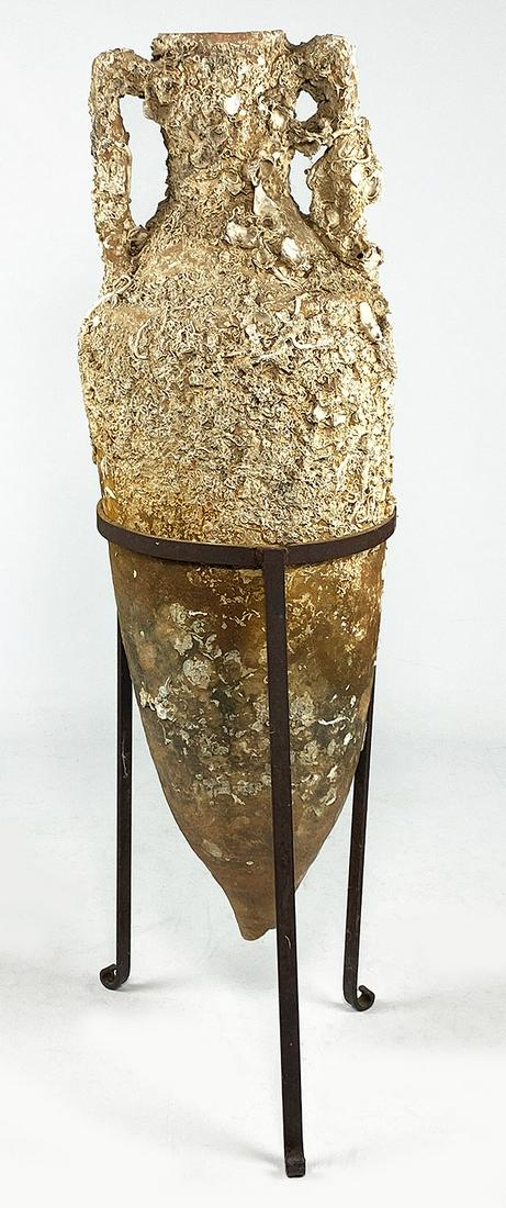 LARGE ROMAN SEA-SALVAGED AMPHORA: with sea encrustations, set in custom iron stand, vase 37"h; in stand 44" h; 13" diam. Amphorae were used for sea transport of wine dating back to the bronze age.