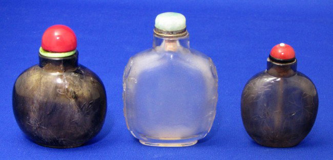 (3) VARIOUS CHINESE SNUFF BOTTLE: rock crystal with carved monkey head sides, 3.25" inc. jade and silver top (spoon missing) small chip to top of neck; smokey quartz with carved blossoms, 3.5" inc. coral top with spoon, small chip on