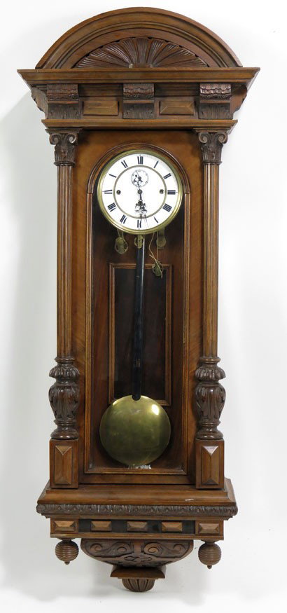 VIENNA WALNUT REGULATOR CLOCK: molded half rounded cornice, carved side columns flanking glazed door, carved drop pendant, enamel dial with Roman numerals, 50”h; 19.5”widest
