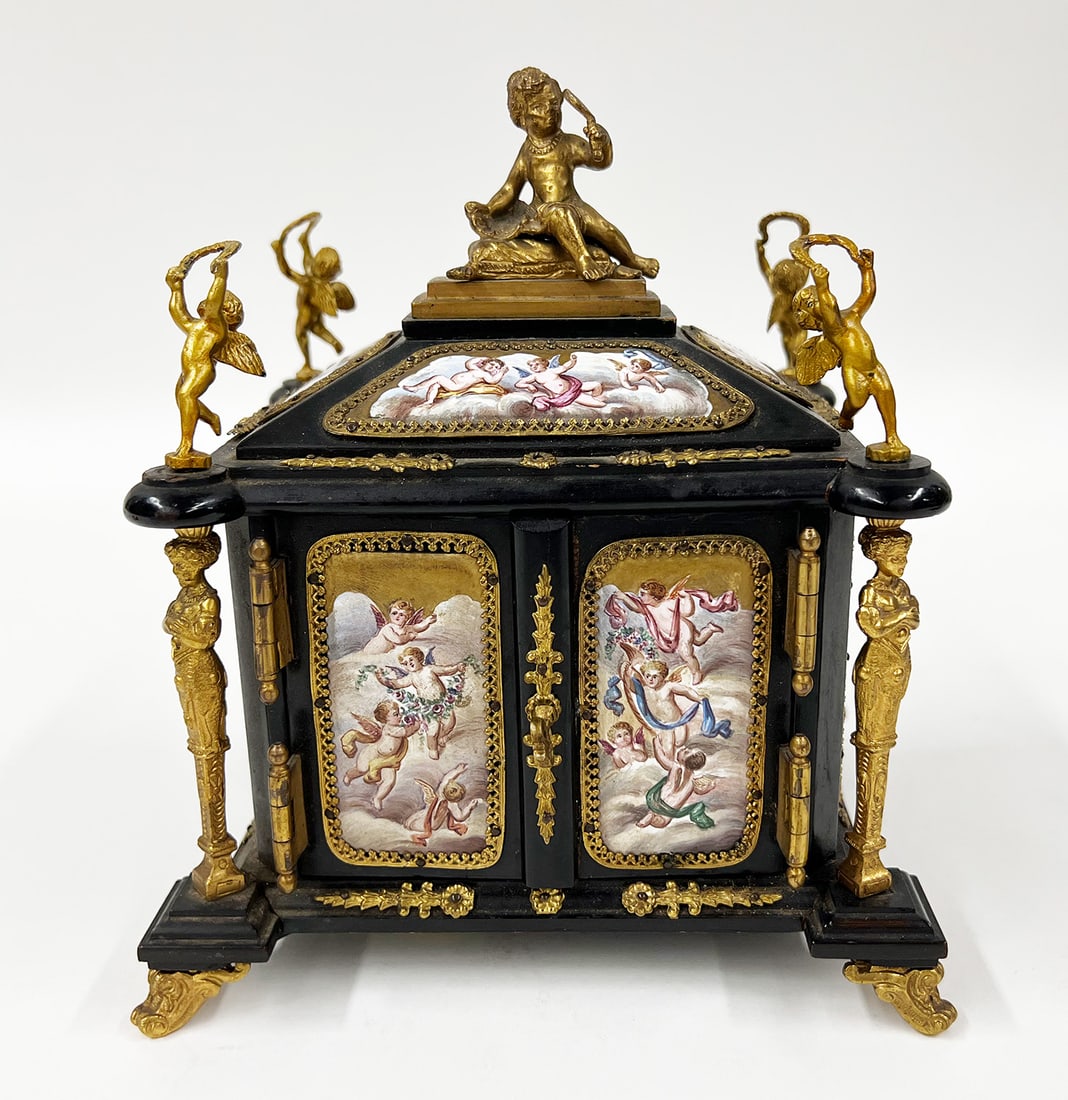 AUSTRIAN/VIENNESE ENAMEL, ORMOLU AND EBONIZED CASKET: overall abundant enamel plaques depicting Greek figures and cherubs; the overhanging top of case surmounted by ormolu putto holding a mirror; each corner mounted with an ormolu dancing cherub, support