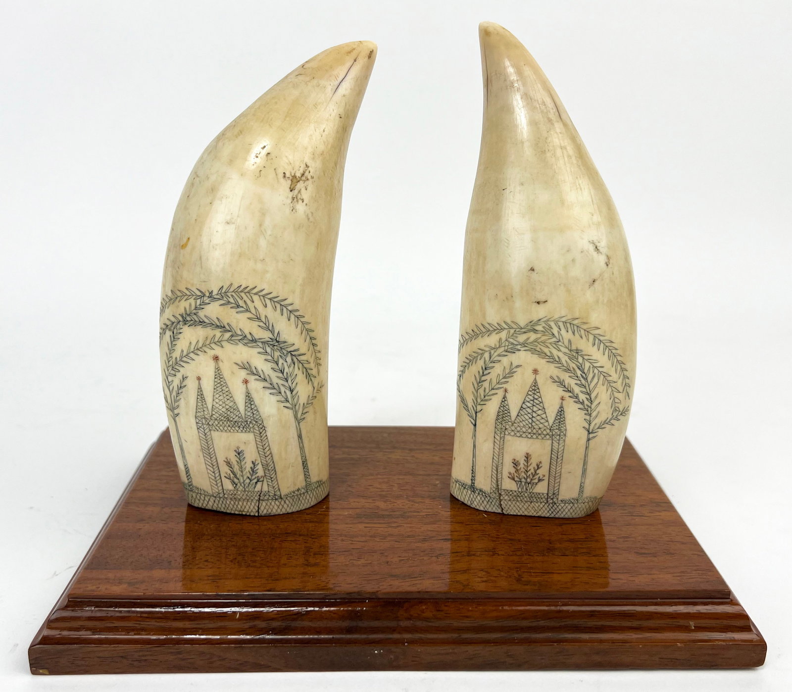 PAIR OF 19TH C. SCRIMSHAW WHALE TEETH: each with identical decoration of a garden structure beneath weeping willows; hatchcross band at base; 6"; 2" at base; on wood base (not attached) NOTE: Apologies, we cannot approve