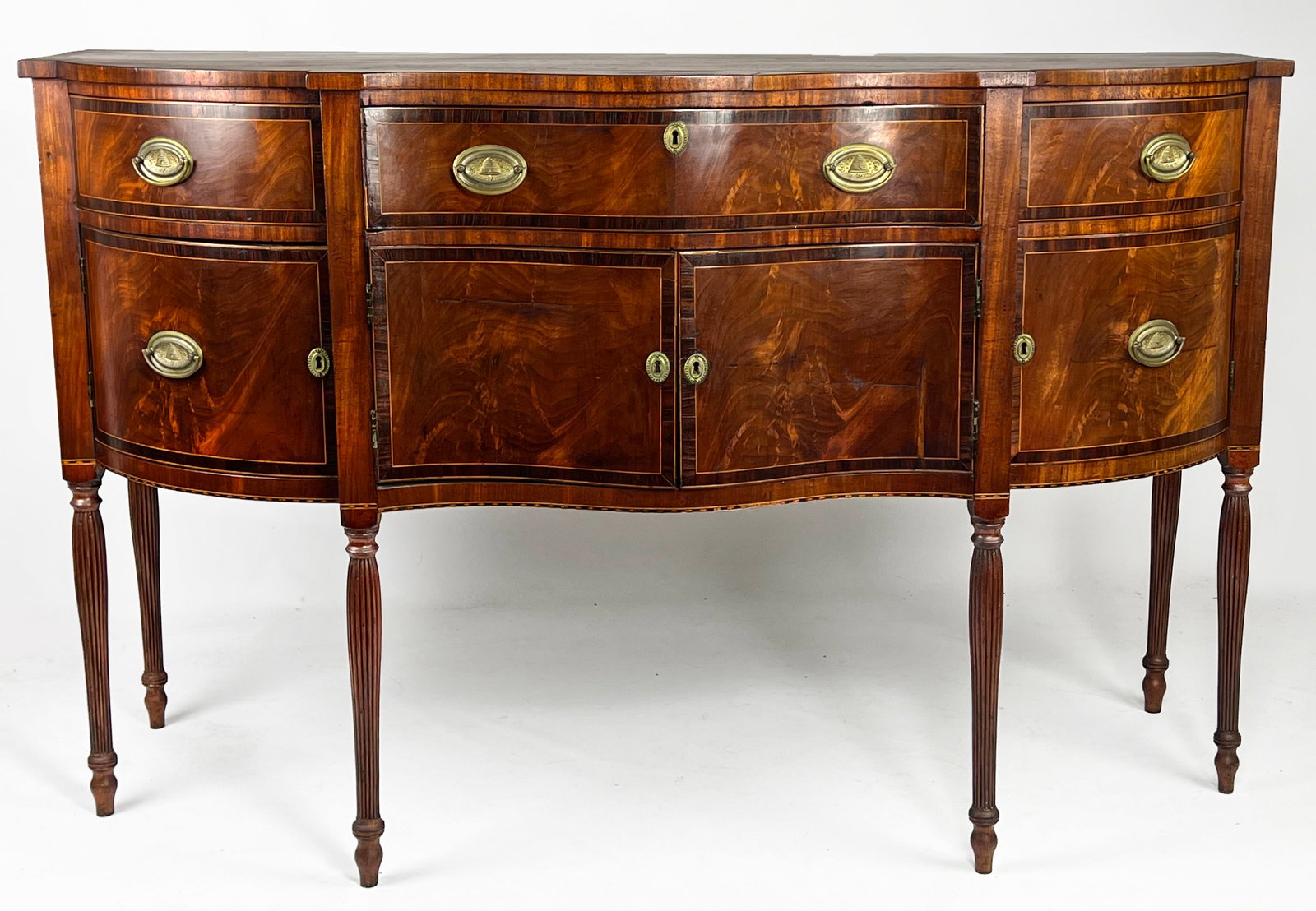 NEW ENGAND HEPPLEWHITE INLAID MAHOGANY SIDEBOARD: serpentine front with bowed ends; three drawers over four doors with band and line inlay; six tapering, fluted legs; 40.75"h; 65"w; 25.5"d From a Providence, RI family. NOTE: Apologies, we cannot appr
