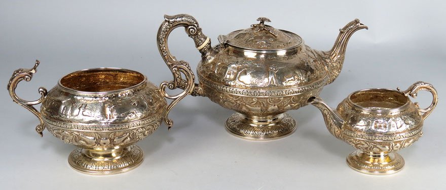 (3) GEORGIAN SILVER TEA SET: Alice and George Burrows, London, 1816 elaborate repousse decoration of fruit and foliage below a banded middle with hunter in landscape above; consisting of a teapot, open sugar and creamer, 48 troy