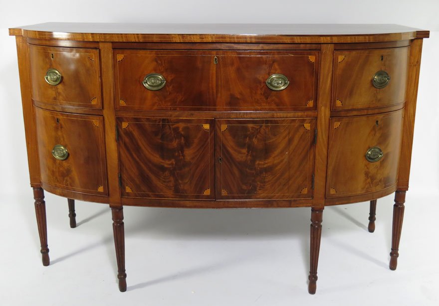 BOSTON SHERATON INLAID MAHOGANY BOWFRONT SIDEBOARD: bowed apron drawer flanked by bowed side drawers, above pair of doors flanked by bowed liquor drawers all with fan inlay to each corner, oval lion embossed brass, on tapering reeded legs, 40.5”h; 62