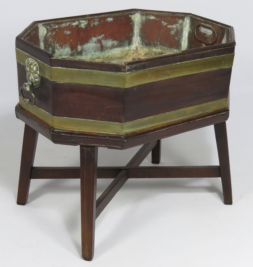 ENGLISH REGENCY OVAL MAHOGANY WINE COOLER: open octagonal-form, double brass bands and with lion head brass handles, original copper liner and splay-leg stand, 23”h; 26.5”w; 19.5”d