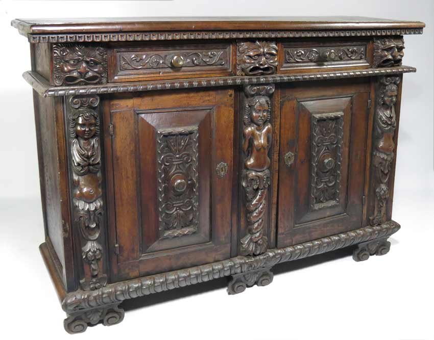 RENAISSANCE CARVED WALNUT CREDENZA: Tuscany, pair of carved frieze drawers alternating with short drawers carved with masques, above a pair of carved paneled doors centered and flanked by carved terms, molded base on shell carved scroll