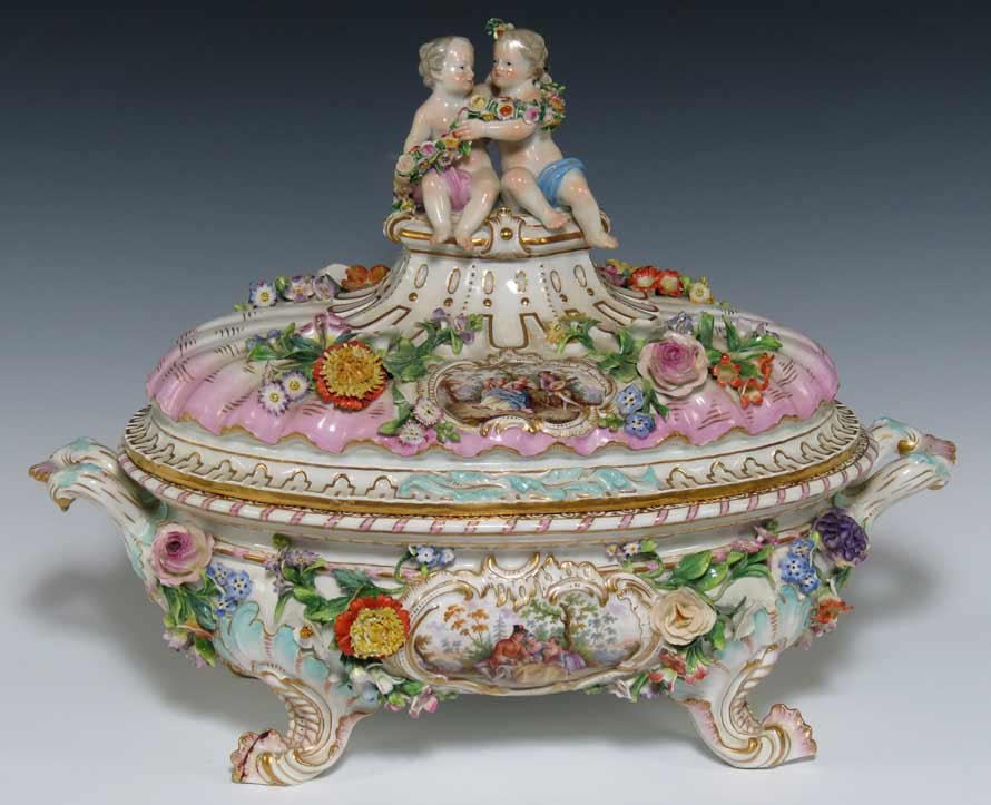 MEISSEN OVAL COVERED TUREEN: 19th c., blue crossed swords mark, also orange 3. finial being a pair of putto holding a floral garland, applied florals to lid and body, painted medallions of courtly figures in a landscape to front
