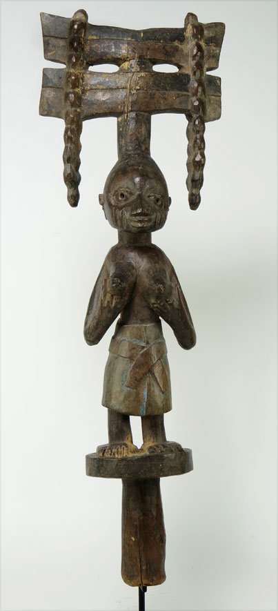 YORUBA SHANGO STAFF: Nigeria, carved wood, standing female wearing elaborate headdress, traces of blue pigment on skirt, 19”; 6”w, on stand The David Abbate (1949-2013) Collection