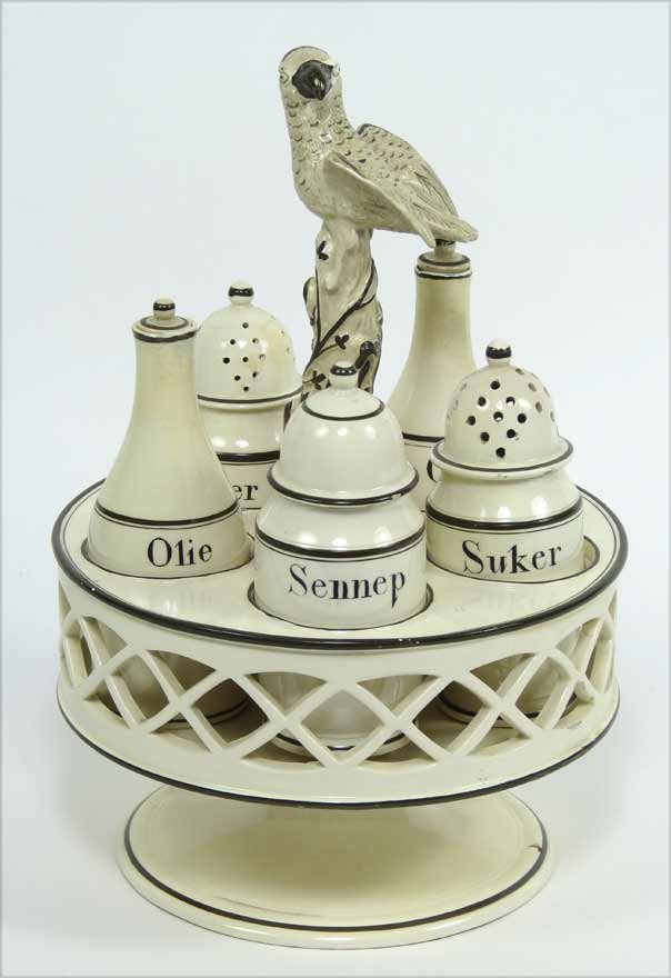 FRENCH CREAMWARE CRUET SET IN STAND: handle a parrot perched on tree, five various bottles labeled in brown glaze, set in reticulated round footed stand, brown glaze banding, 10.5”h; 7”diam.