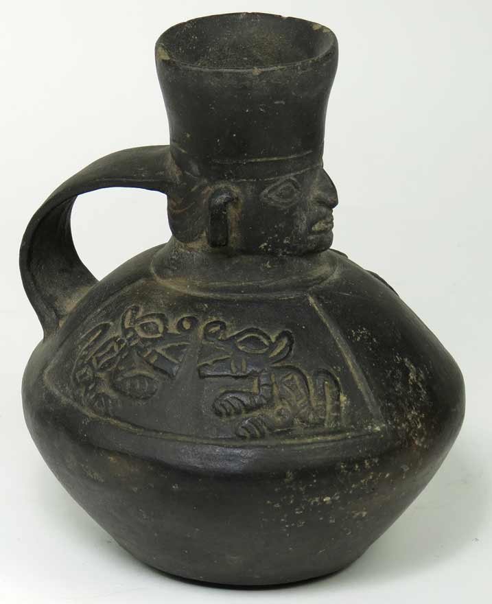 PRE-COLUMBIAN TERRA COTTA VESSEL: black glaze, single handle with sculpted mask to neck, panels of animals to body, 8.5”, old collection sticker on base, also on base, faint D.L.L. Ex. Kurt Reynolds collection, Boston