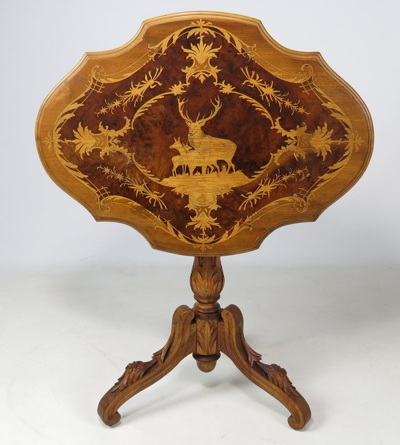BLACK FOREST CARVED AND MARQUETRY TIP-TABLE: late 19th c., area of Brienz and Interlaken shaped oval tilting-top with marquetry stag, doe and fawn encircled by edelweiss flowers set in a burl panel, on foliate carved pedestal with in-scrolling c