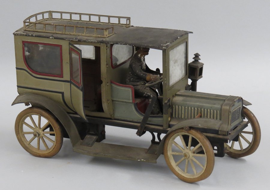 CARETTE TIN LIMOUSINE: c. 1910, clockwork driven driver and three passengers, one a child; roof rail, beveled windows and rubber tires, 6.75”h; 11.5”long The consignor’s mother and father collected dolls and toys for