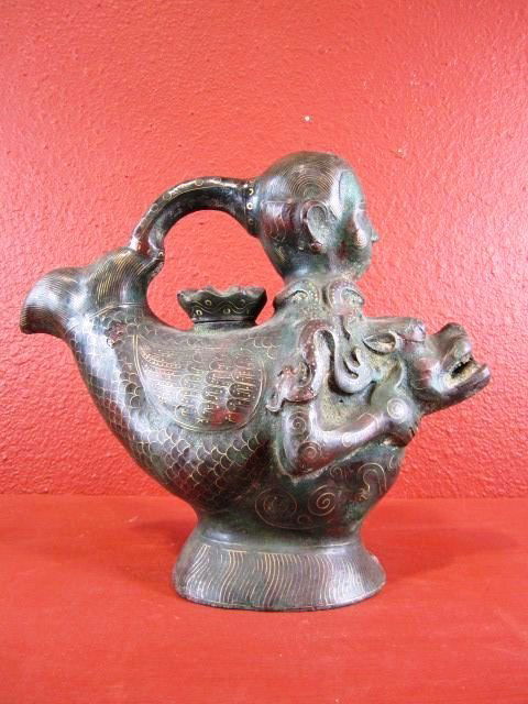 Chinese Bronze Statue of the 19th Century: Oriental metalware vessel in the form of a boy riding on a fish. The fish has inlaid gilt metalwork as does the figure of the boy, there is a lotus flower head stopper in the back of the fish and the