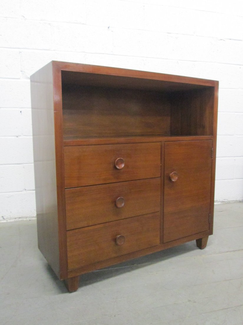 Art Deco Cabinet / Bookcase style of Gilbert Rohde: Art Deco walnut cabinet / bookcase with three pull out drawers and a cabinet door. Handles are walnut as well. In the manner of Gilbert Rohde. Measures: 36"W x 14.5"D x 37.5"H.