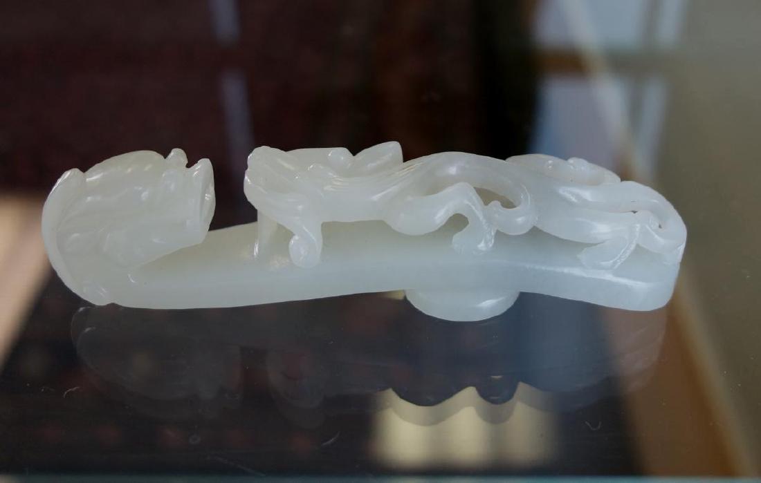 Chinese Carved White Jade Belt Hook: A Chinese carved white to very faint grey jade belt buckle or hook. Finely carved depicting a dragon head terminal, with hydra / chilong in relief to the shaft. Measures 4" long, 1" high, .75" deep.