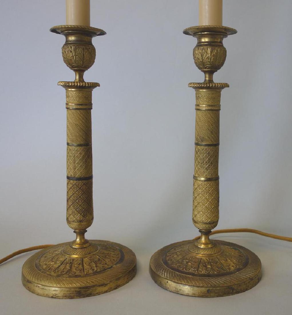 French Gilt Bronze Candlesticks / Lamps: A pair of French gilt bronze candlesticks / lamps. Electrified for use as lamps. Acanthus leaf and geometric motif. Overall 31.75" high to top of harp finial, 5.25" diameter at the base. NOTE: can eas