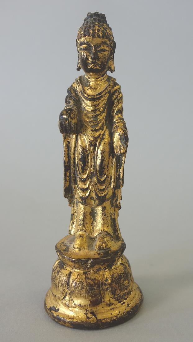 Korean Gilt Bronze Buddha: A Korean gold gilded bronze sculpture of Buddha, 19th century. The "travel" bronze depicts Buddha standing on a lotus formed base, hands gesturing and holding a ball. Measures 4.25" high, 1.5" diamete