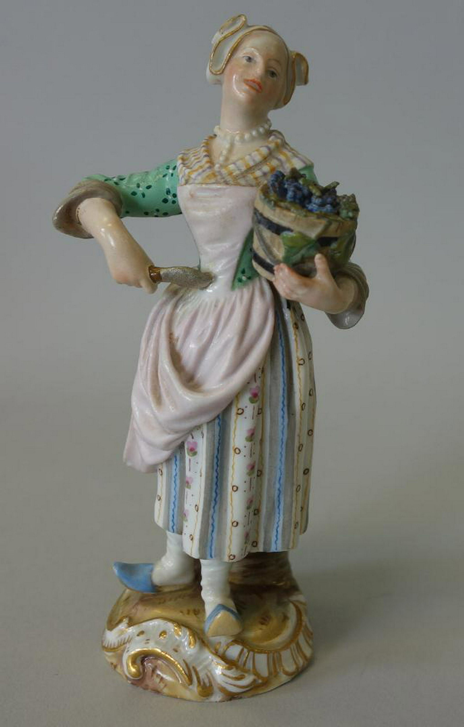Meissen Porcelain Figure, The Gardener: A fine 19th century Meissen porcelain figure of a young woman holding a basket of flowers over one arm, and holding a spade shovel in her right hand, "The Gardener". Signed on the underside with the C