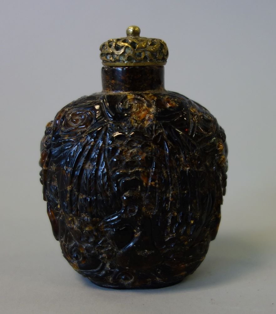 Chinese Carved Amber Snuff Bottle: A Chinese carved amber snuff bottle. Well hollowed and finely carved depicting a phoenix bird on the two opposing sides. The short sides decorated with temple lions / mythological beast faces. Measure
