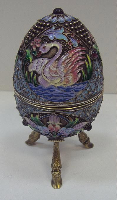 Russian Silver 84 Enamel & Jeweled Egg Box: The egg is decorated with three swans surrounded by bright enamels in silver wire work and rests on three hoofed feet. Seven semi-precious cabochon stones (garnets) further adorn the egg box. Measures