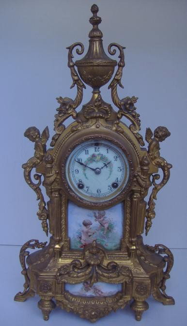 New Haven Gilt-Metal Clock with Putti: Elaborate gilt metal clock with porcelain face and two porcelain panels of putti at play. Each side of the clock is adorned with winged putti. Measures 18.5" tall, 10.5" wide and 3.75" deep. (Missing 
