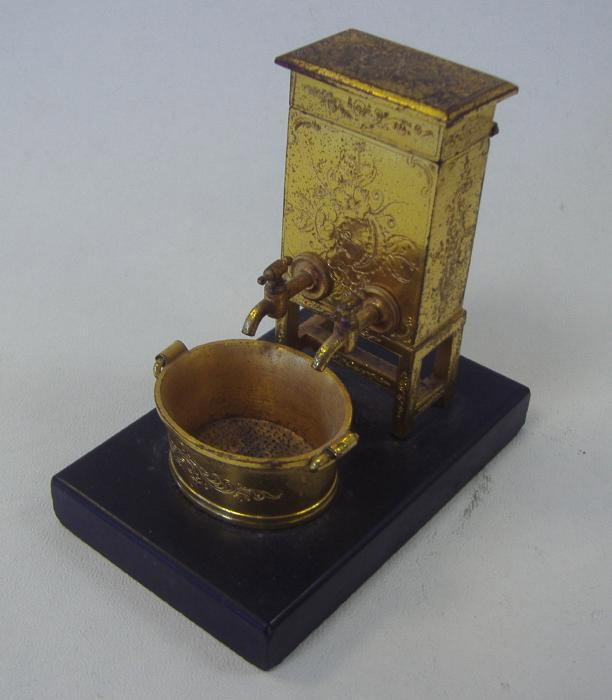19thc Miniature Commode Gilt Metal Match Safe: Gilt-metal match safe in the form of a double faucet commode with a wash basin as the receptacle. Mounted on slate. Overall height, 3.5". The base measures 2.25" x 3.5". Quite unique.