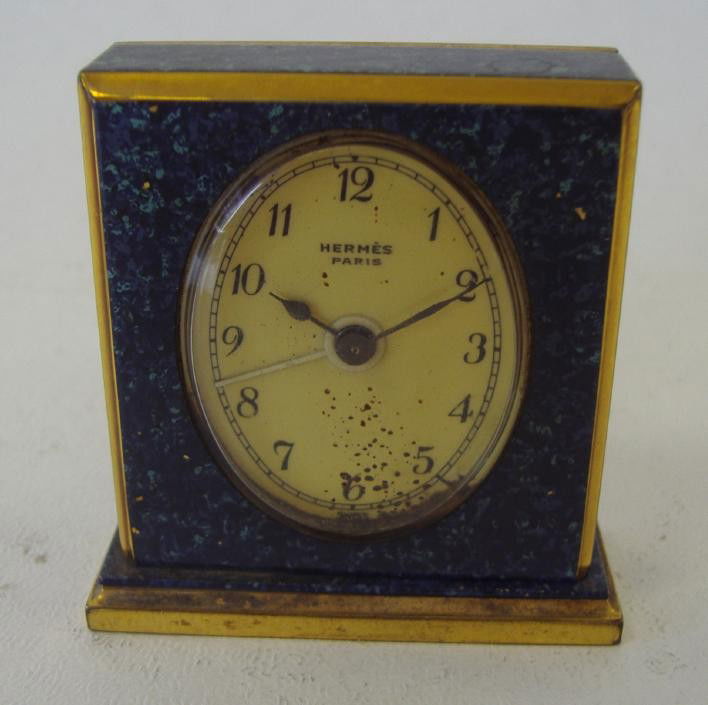 Hermes Paris Swiss Travel Clock: Hermes travel clock with a blue stone and gilt bronze case. Measures 2" tall, 2" wide and 1/2" deep. NOTE: one loose-missing screw at base, paint specks on crystal and not currently in working order.