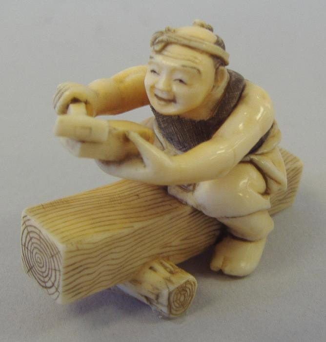 Japanese Ivory Carved Netsuke of Carpenter,signed: Carved ivory and polychromed figural netsuke of a carpenter working astride a wood log, signed. Measures 1.78" in length.