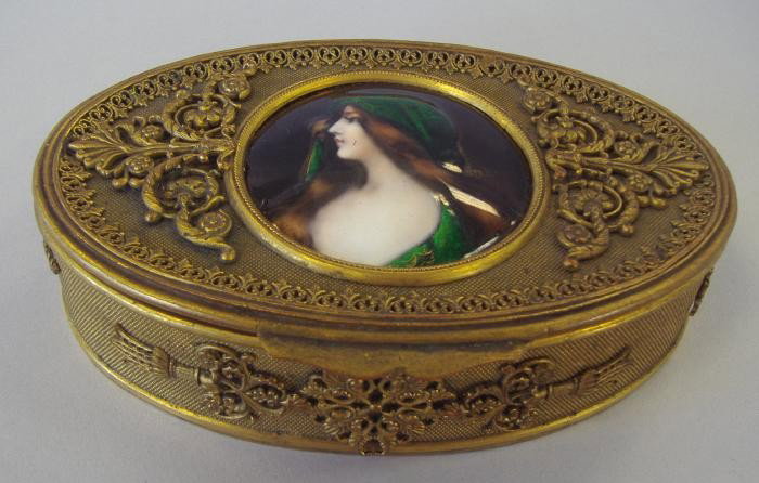 Brass & Enamel Portrait Jewel Box: French brass oval jewel box. The lid inset with an enamel painted plaque of a veiled young woman. The plaque measures 2" in diameter. The velvet lined box measures 5" wide, 3.25" deep and 1-3/8" high.