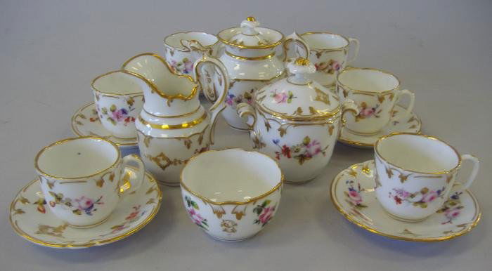 French Porcelain Child's Tea Set, 16 pieces: Hand-painted porcelain cild's tea set comprised of a teapot measuring 3.5" tall, a covered sugar bowl, cream pitcher, waste bowl, and six cups with saucers. The saucers measure 3.75" in diameter. The