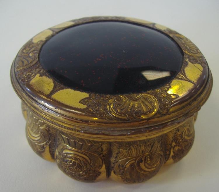 Brass & Heliotrop Bloodstone Jasper Snuff Box: Etched brass box with a shell and floral motif. The lid inset with a large heliotrop or bloodstone, measuring 2-1/8" in diameter, (green jasper with red spots). The box measures 3" in diameter and 1.5