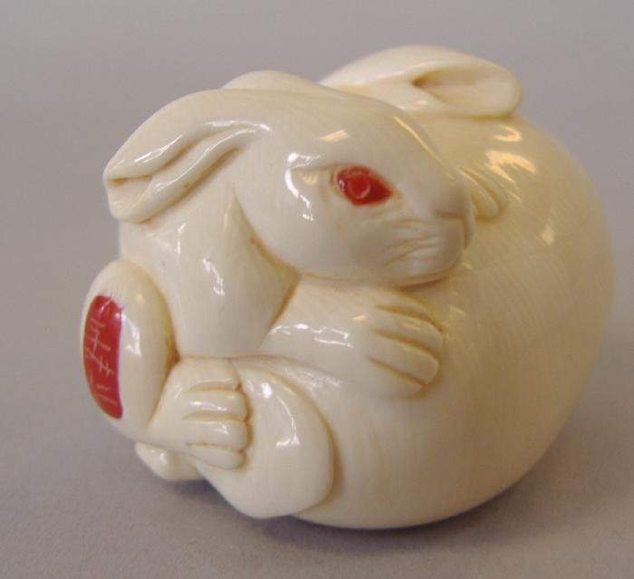 Carved Ivory Netsuke, Two Rabbits, signed: Carved ivory netsuke depicting a baby rabbit climbing on the back of a larger rabbit. Both with inlaid red eyes. Signed. Measures 1" high, 1-5/8" long and 1.25" wide.