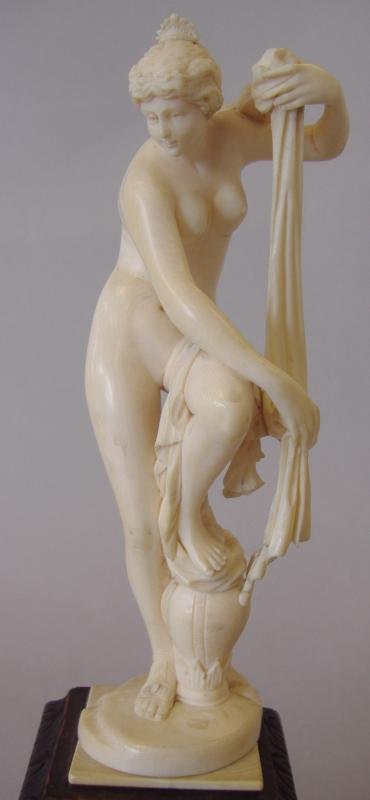 Carved Ivory Model of a Female Nude, Goddess Venus: Carved ivory model of Goddess Venus at her bath. This female nude sculpture measures 5.5" high. Mounted on a carved wood stand, with an overall height of 8".