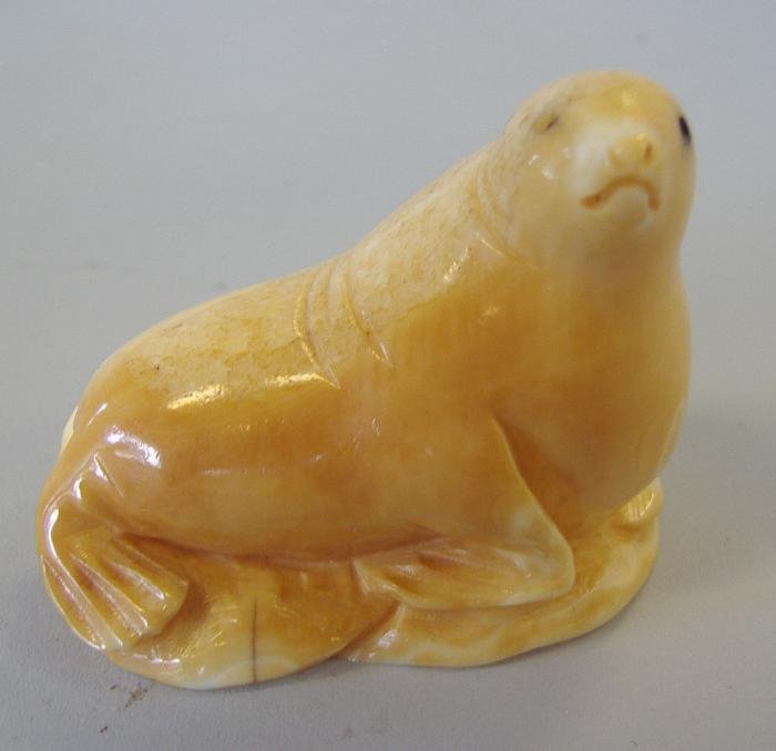 Inuit Walrus Ivory Carving of a Seal, Eddy Symzoi: Inuit ivory carving of a seal. Measures 2" high, 2" long and 1.25" wide. Signed Eddy Symzoi? Comes with a plexiglass stand.