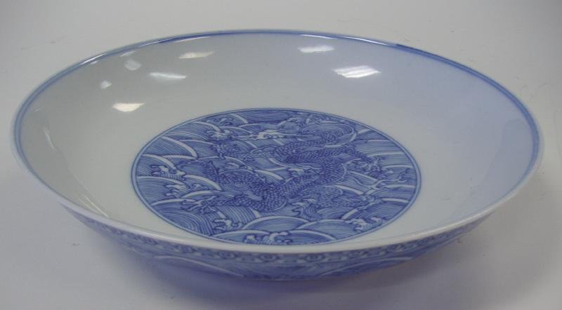 Chinese Blue & White Porcelain Dragon Dish, Signed: Chinese porcelain dish or shallow bowl, decorated in underglaze blue enamels depicting a five claw dragon in the center. The exterior decorated with a band of dragons within a wave motif. Measures 8.2